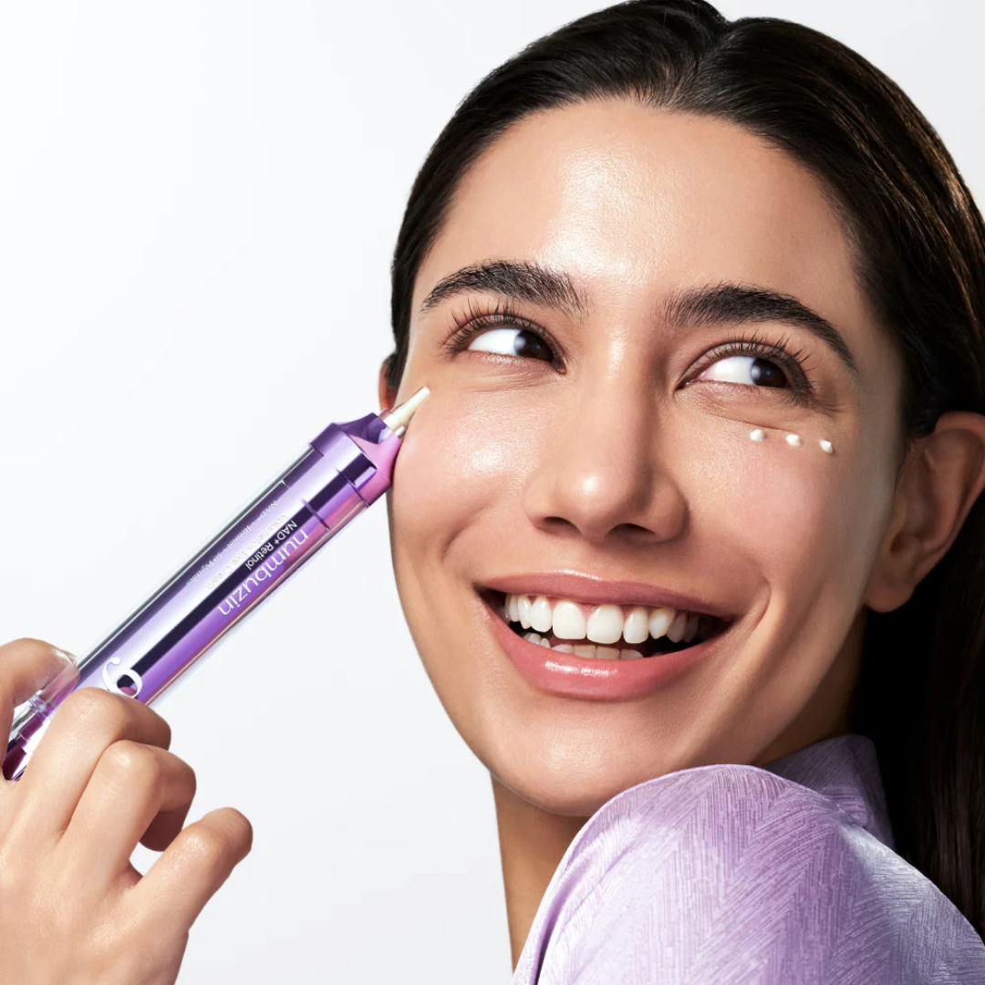 Woman applying a cosmetic product to her face with a purple applicator.
