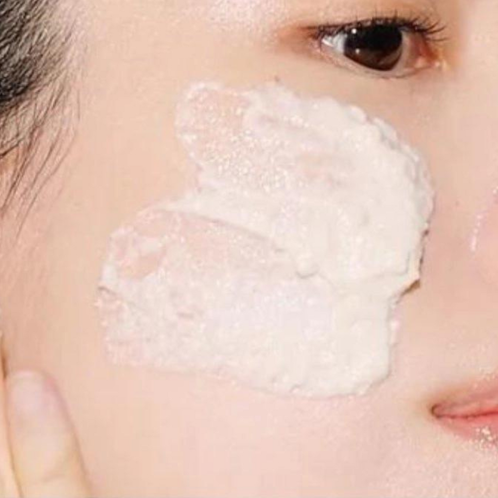 Close-up of a person applying a white cream or foam to their face.