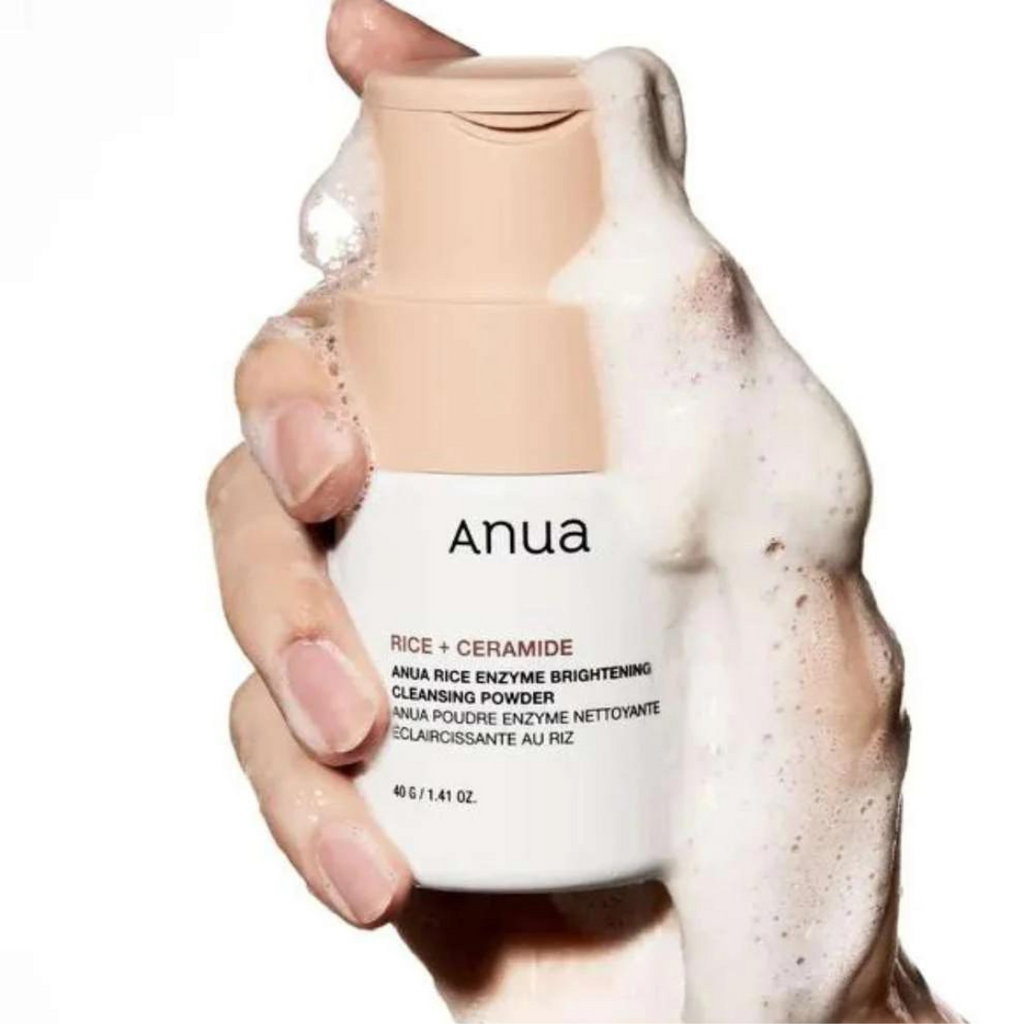 Hand holding a bottle of Anua cleansing powder with foam on a white background