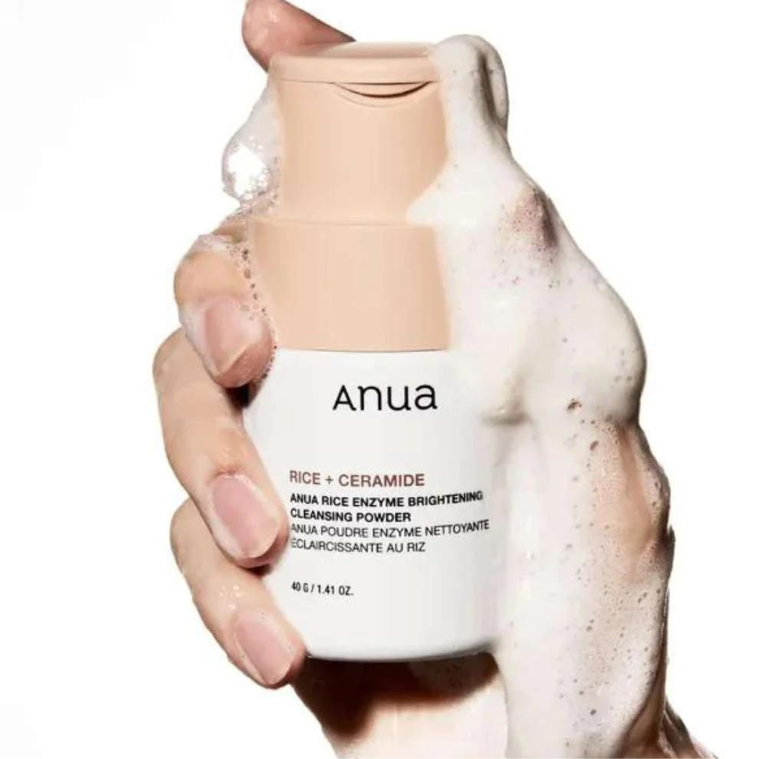 Hand holding a bottle of Anua cleansing powder with foam on a white background